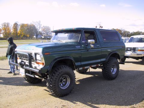 1993 Ford Bronco - Lifted green Ford Bronco with flame decals and a front bull bar is parked next to another truck.