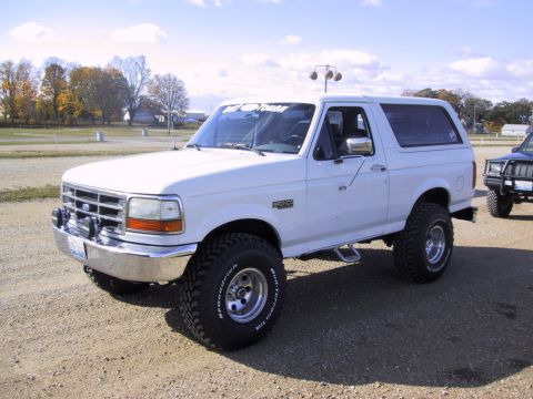 1993 Ford Bronco - A white Ford Bronco is parked on a dirt lot with a second vehicle visible in the background.