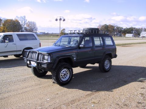 1993 Ford Bronco - A dark green Jeep Cherokee is parked next to a white Ford Bronco on a sunny day.