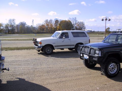 1993 Ford Bronco - A white 1993 Ford Bronco is parked on a gravel lot next to another SUV under a clear sky.