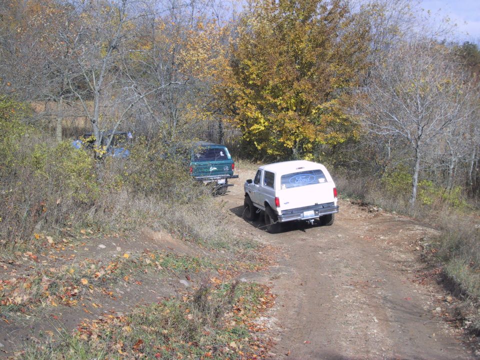 1993 Ford Bronco and a green SUV on a dirt road during fall
