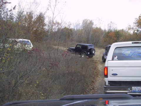 1993 Ford Bronco - A white Ford Bronco is seen from the rear, following other vehicles on a dirt road.