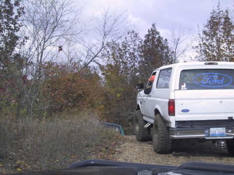 1993 Ford Bronco - A white 1993 Ford Bronco is seen from the rear on a dirt road surrounded by autumn foliage.