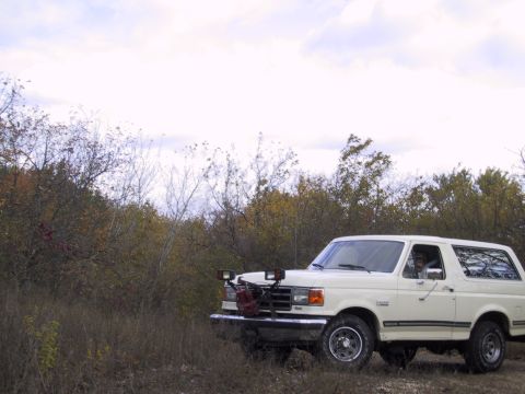 1993 Ford Bronco - White 1993 Ford Bronco with auxiliary lights and a red gas can on the front bumper, parked in a grassy, wooded area.