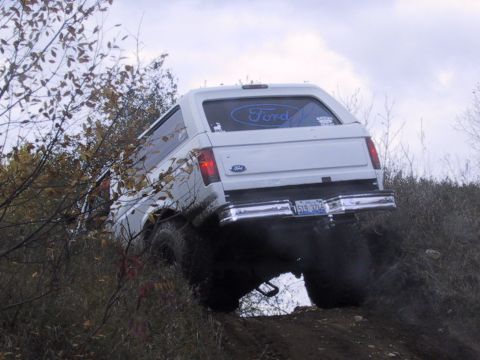 1993 Ford Bronco - A white 1993 Ford Bronco navigates an off-road trail, kicking up dirt as it climbs.