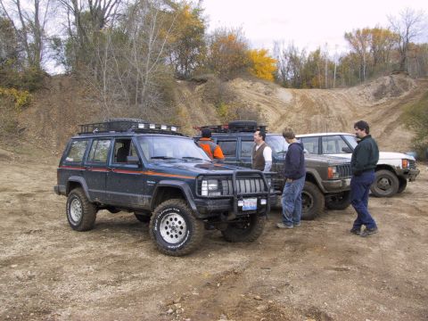 1993 Ford Bronco - Several off-road vehicles, including Jeep Cherokee XJs and a Range Rover Classic, are parked together on a dirt trail.