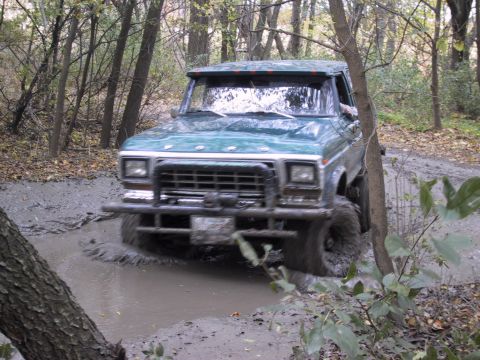 1993 Ford Bronco - A green Ford Bronco navigates a muddy trail in a wooded area.