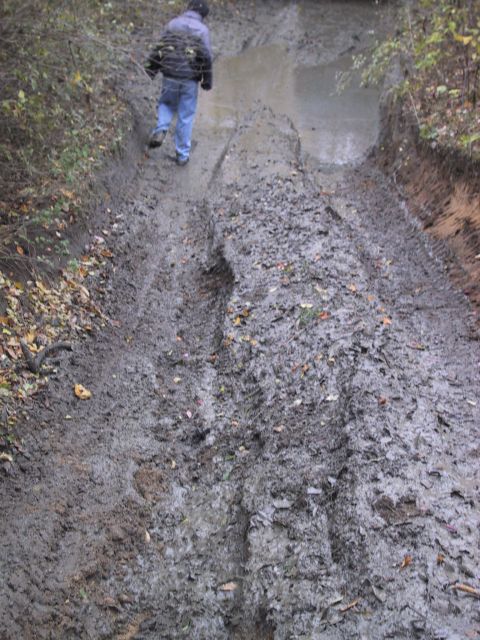 1993 Ford Bronco - A person walks away from the camera on a treacherous, muddy trail, leaving deep tire tracks behind.