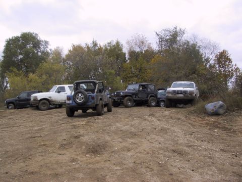 1993 Ford Bronco - A collection of Jeeps and trucks are gathered on a muddy terrain under a cloudy sky.