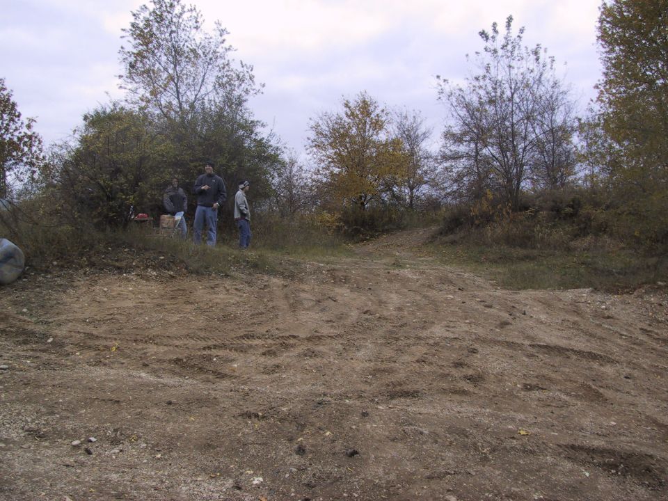 Four people stand on a dirt hill with trees in the background