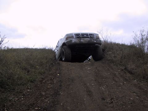 1993 Ford Bronco - A Ford F-Series truck navigates a steep, muddy incline with its front wheels airborne.
