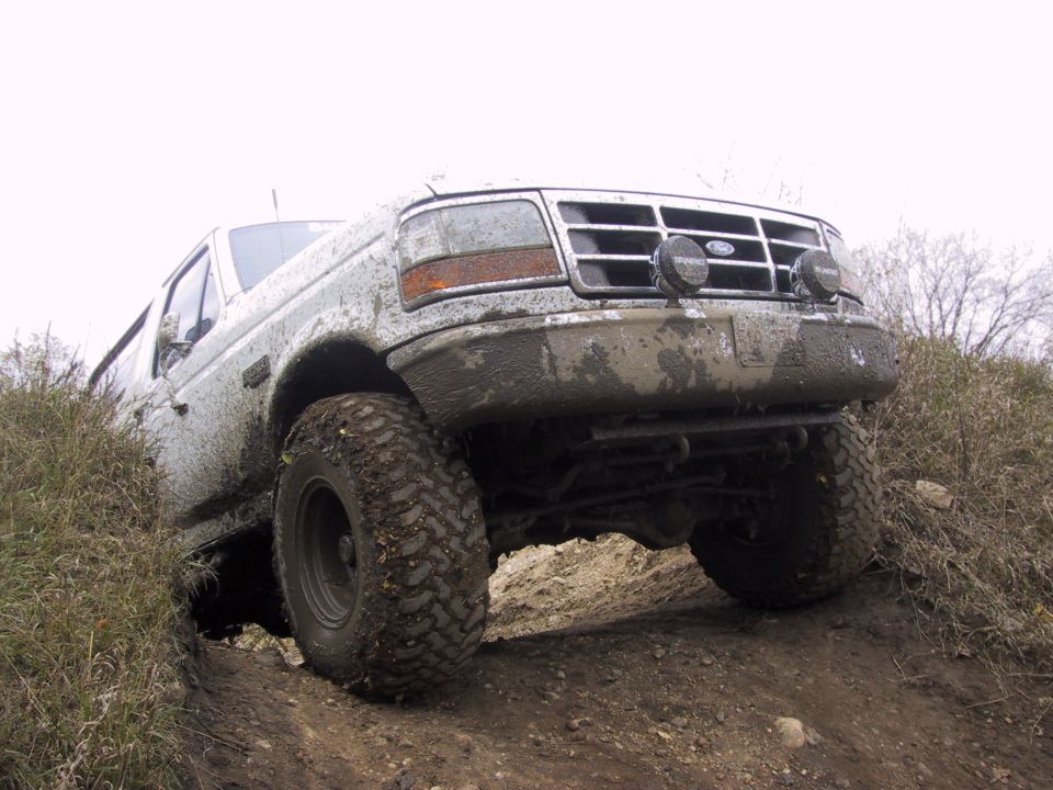 Mud-covered 1992 Ford Bronco driving off-road, front 3/4 view