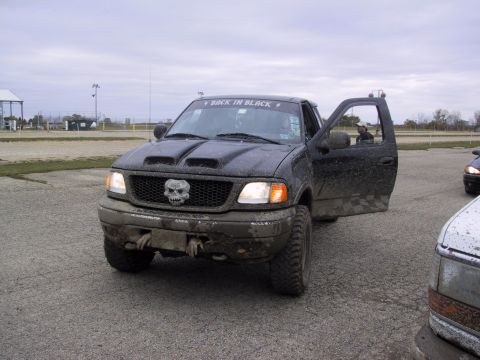 1993 Ford Bronco - A muddy black Ford F-150 truck with a skull emblem on the grille and 'BACK IN BLACK' sticker on the windshield.