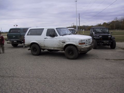 1993 Ford Bronco - A muddy white Ford Bronco is parked on asphalt, with other vehicles in the background.