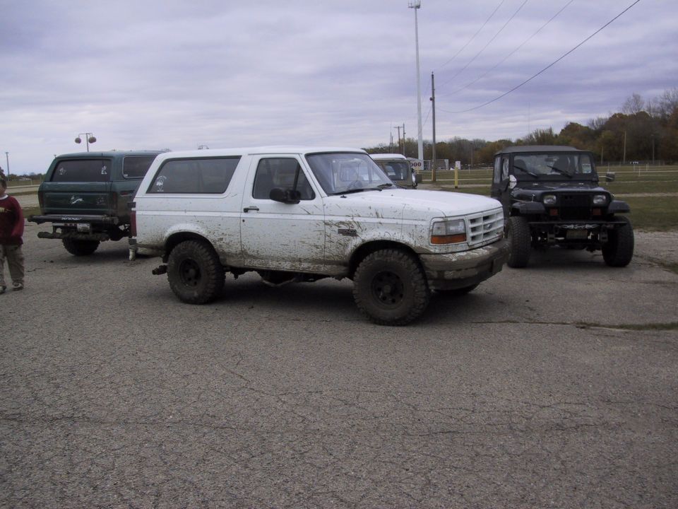 White Ford Bronco covered in mud, parked on asphalt with other vehicles
