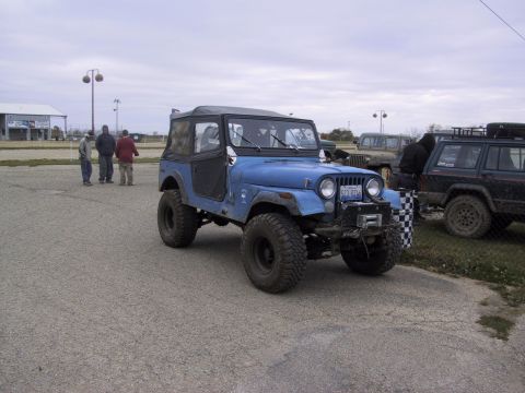 1993 Ford Bronco - A blue Jeep CJ-7 with a soft top and winch is parked in a lot with other vehicles and people.