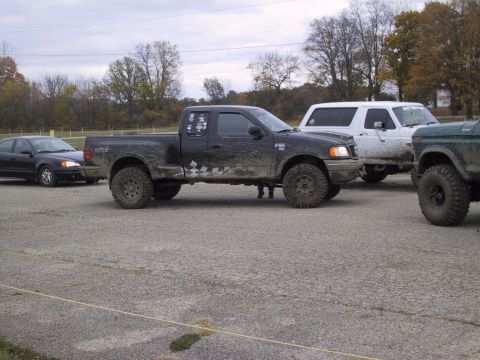 1993 Ford Bronco - Several trucks and SUVs are parked together on a gravel lot under an overcast sky.