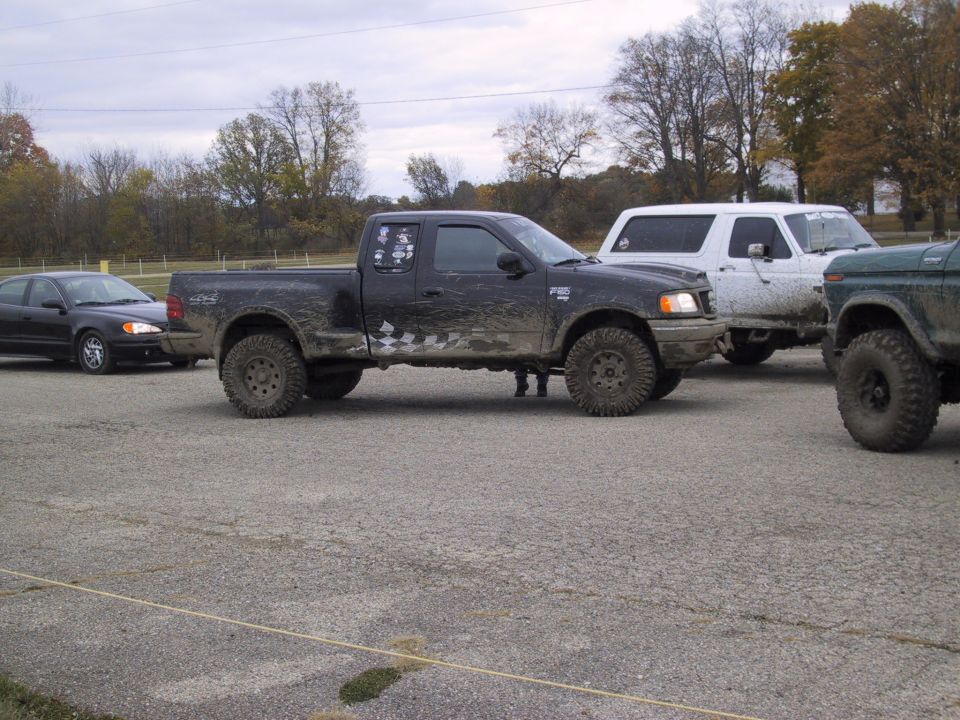 Black pickup truck with lifted suspension and off-road tires, parked next to a white SUV and a green vehicle