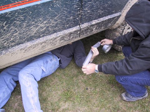 1993 Ford Bronco - Two individuals attempt a roadside repair on a vehicle's exhaust system using duct tape.
