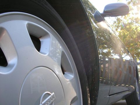 1995 Nissan 240SX - Close-up of a silver Nissan wheel and the side fender of a dark car, with sunlight reflecting off the paint.