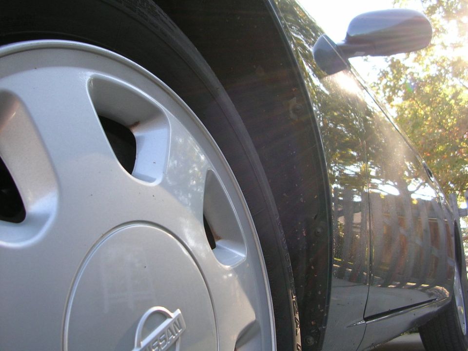 Silver Nissan wheel and dark-colored car fender with sun glare