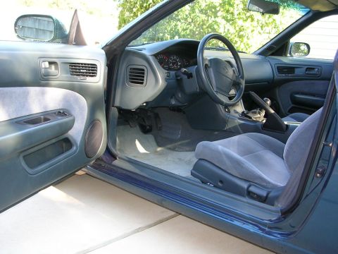1995 Nissan 240SX - The interior of a car is shown with the driver's door open, revealing the grey seats and dashboard.
