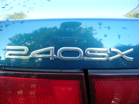 1995 Nissan 240SX - Rear emblem on a teal car reads 240SX. Water droplets are visible on the surface.