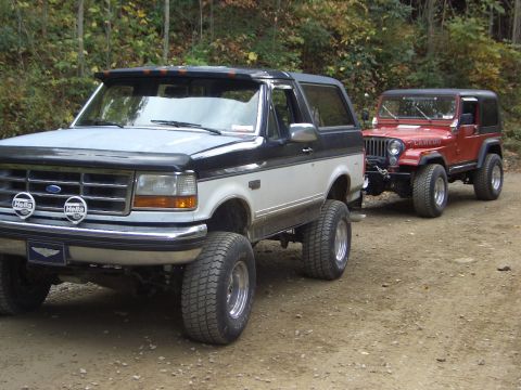 1993 Ford Bronco - A lifted Ford Bronco and Jeep Wrangler are parked on a dirt road, ready for off-road adventure.