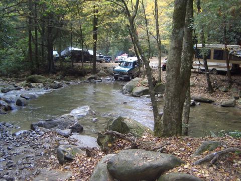 1993 Ford Bronco - A 1993 Ford Bronco navigates a rocky stream bed surrounded by trees and other vehicles.