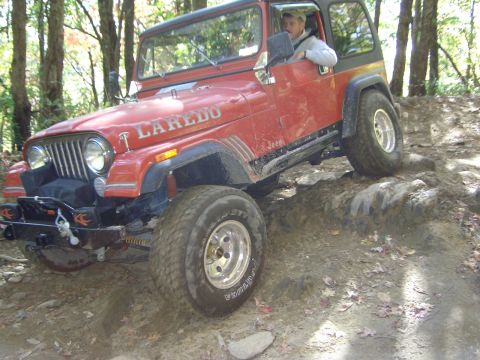 1993 Ford Bronco - This red Jeep Laredo navigates a challenging rocky terrain during an off-road excursion.