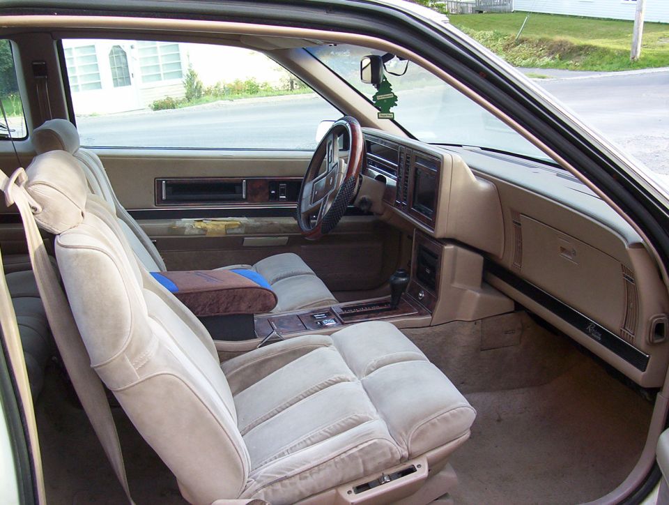 1989 Buick Riviera interior with tan velour seats, wood trim, and a green air freshener hanging from the rearview mirror