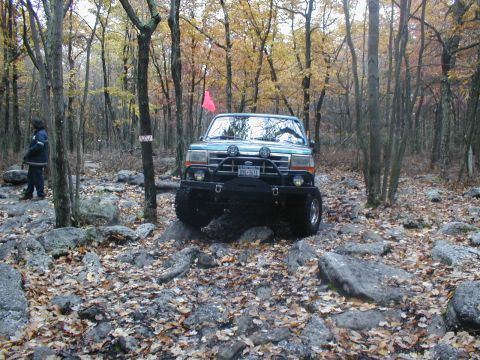 1979 Ford Bronco II - A Ford Bronco navigates a challenging, rocky terrain in a wooded area during autumn.