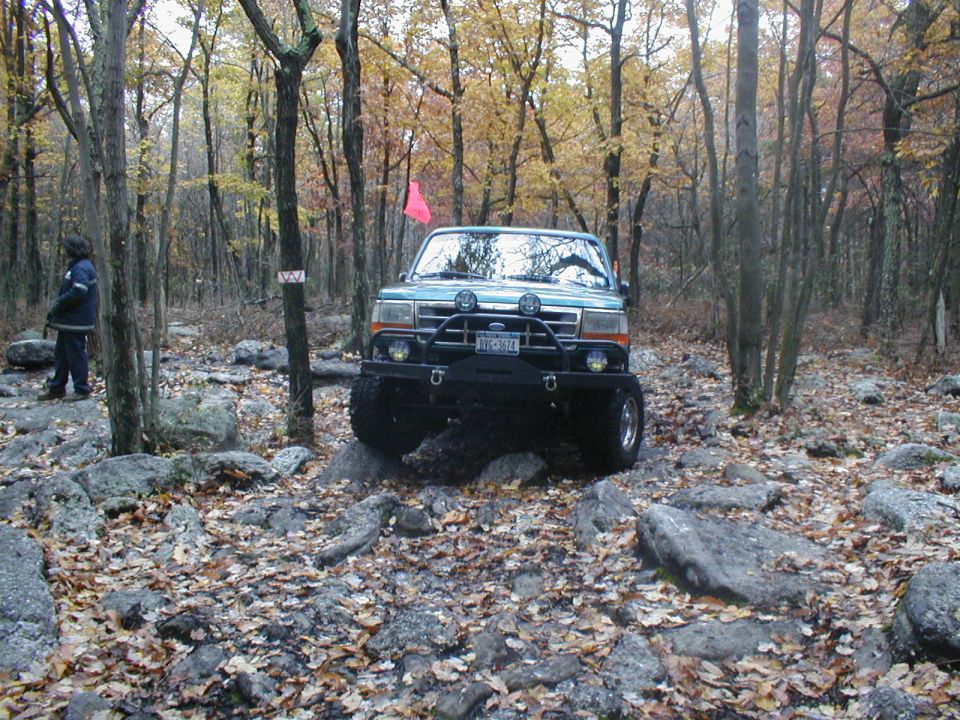 Green Ford Bronco with aftermarket bumper and off-road tires navigating rocks