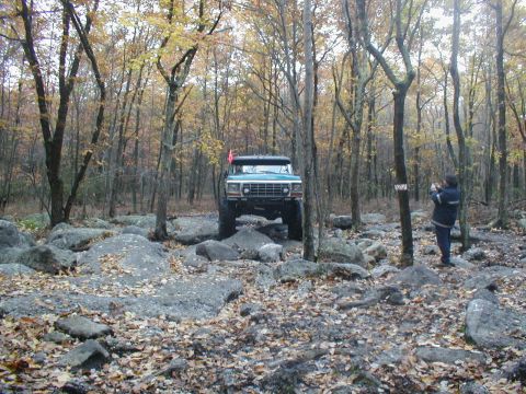 1979 Ford Bronco II - A green 1979 Ford Bronco II navigates a rocky trail in a wooded area during autumn.