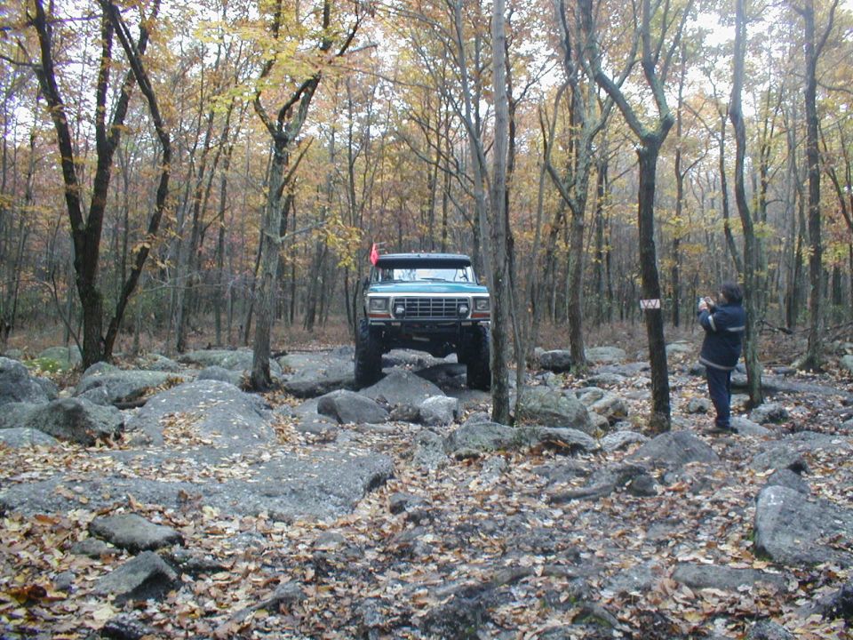Green 1979 Ford Bronco II off-roading over rocks in a forest