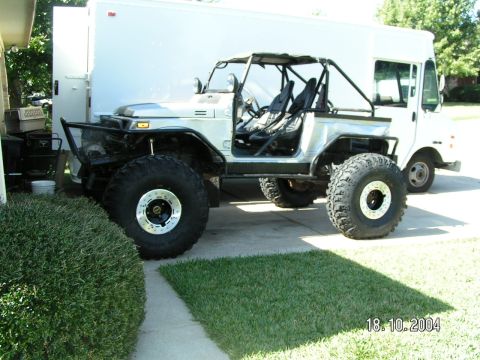 1978 Ford Bronco - This modified vehicle has oversized tires and a roll cage, parked beside a delivery truck.