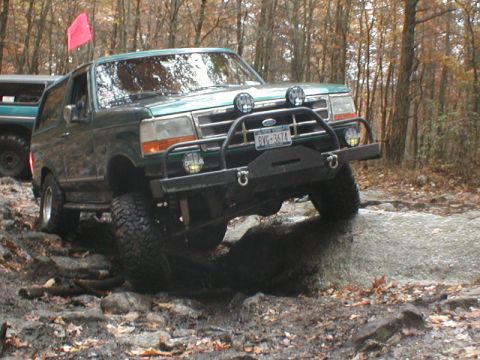 1979 Ford Bronco II - This Ford Bronco navigates a rocky trail with a red flag on top. The vehicle is equipped with a brush guard and auxiliary lights.
