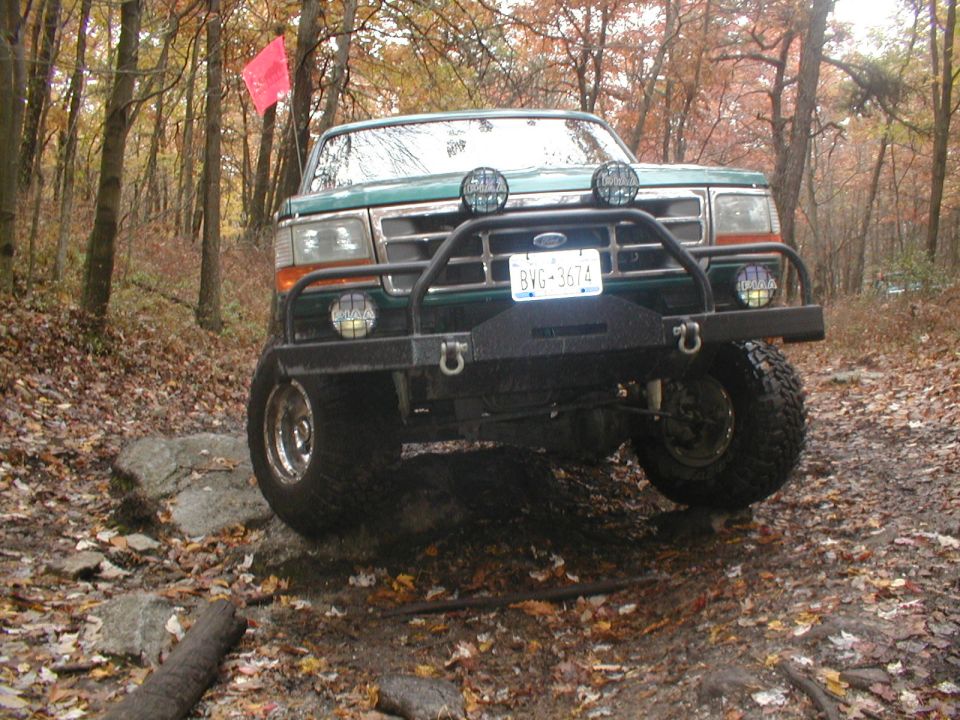 Green SUV on rocky trail, front view. Bull bar, auxiliary lights