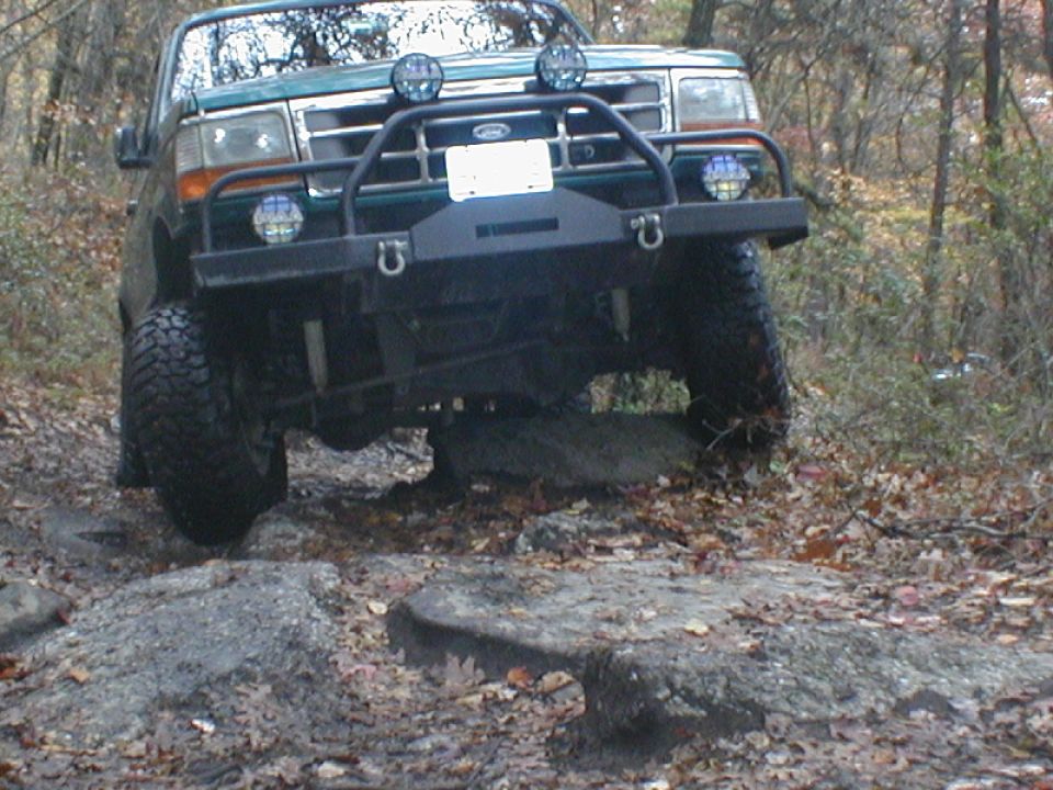 Green Ford F-Series truck with aftermarket bumper and lights navigating rocks on a trail