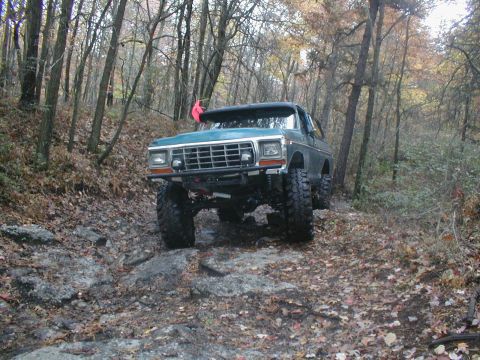 1979 Ford Bronco II - This modified 4x4 navigates a challenging, wooded terrain with large tires and a lifted suspension.