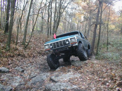 1979 Ford Bronco II - A teal Ford Bronco navigates a challenging rocky terrain in a forest setting.