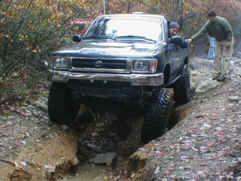 1979 Ford Bronco II - A dark green SUV navigates a challenging off-road terrain with two people observing.