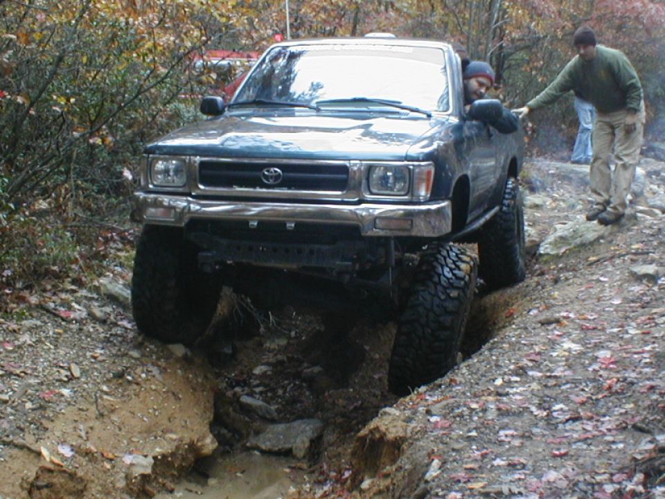 Dark green SUV with lifted suspension and large tires driving through a ditch on a dirt trail
