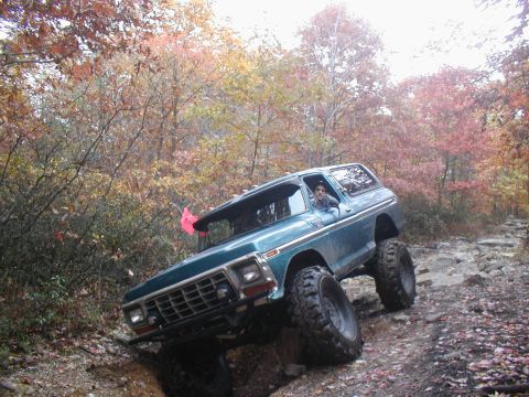 1979 Ford Bronco II - A teal Ford Bronco navigates a challenging rocky path during autumn, with colorful leaves in the background.