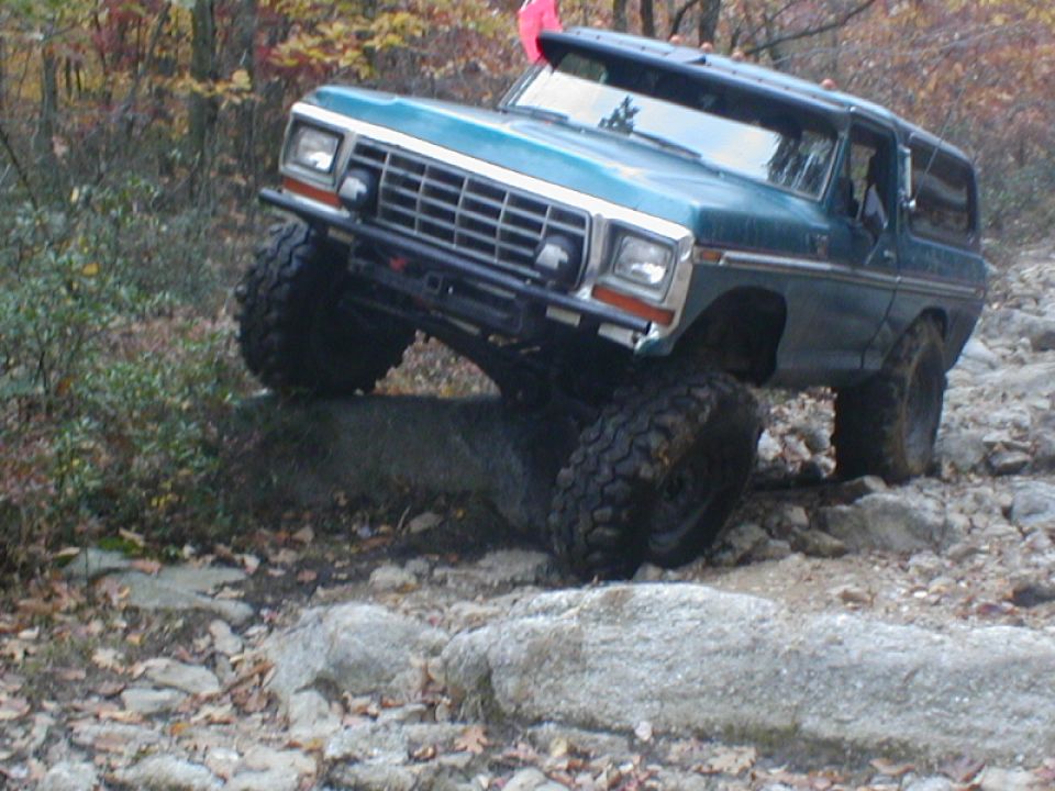 Teal off-road SUV with large tires navigating rocky terrain. Front grille and headlights are visible