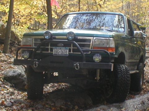 1979 Ford Bronco II - Green 1992 Ford Bronco navigates a rocky, wooded trail with aftermarket bumper and auxiliary lights.