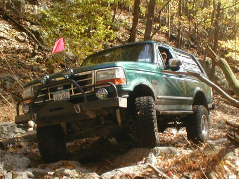 1979 Ford Bronco II - This green SUV navigates a challenging rocky trail, equipped with off-road lights and a custom bumper.