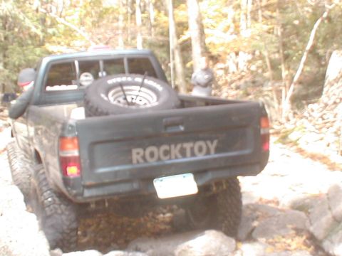 1979 Ford Bronco II - Pickup truck with 'ROCKTOY' tailgate lettering and spare tire in bed is off-roading.