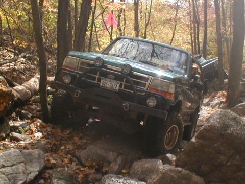 1979 Ford Bronco II - A green Ford Bronco navigates a challenging rocky trail surrounded by autumn trees, with another vehicle visible behind it the background.