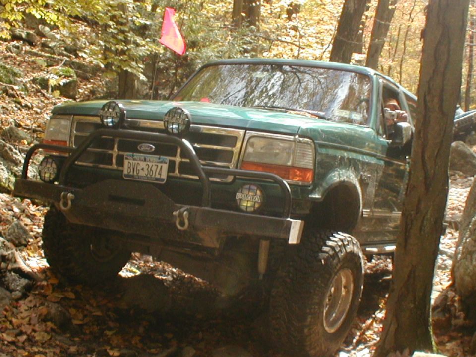 Green Ford Bronco with off-road bumper and lights navigating a rocky trail
